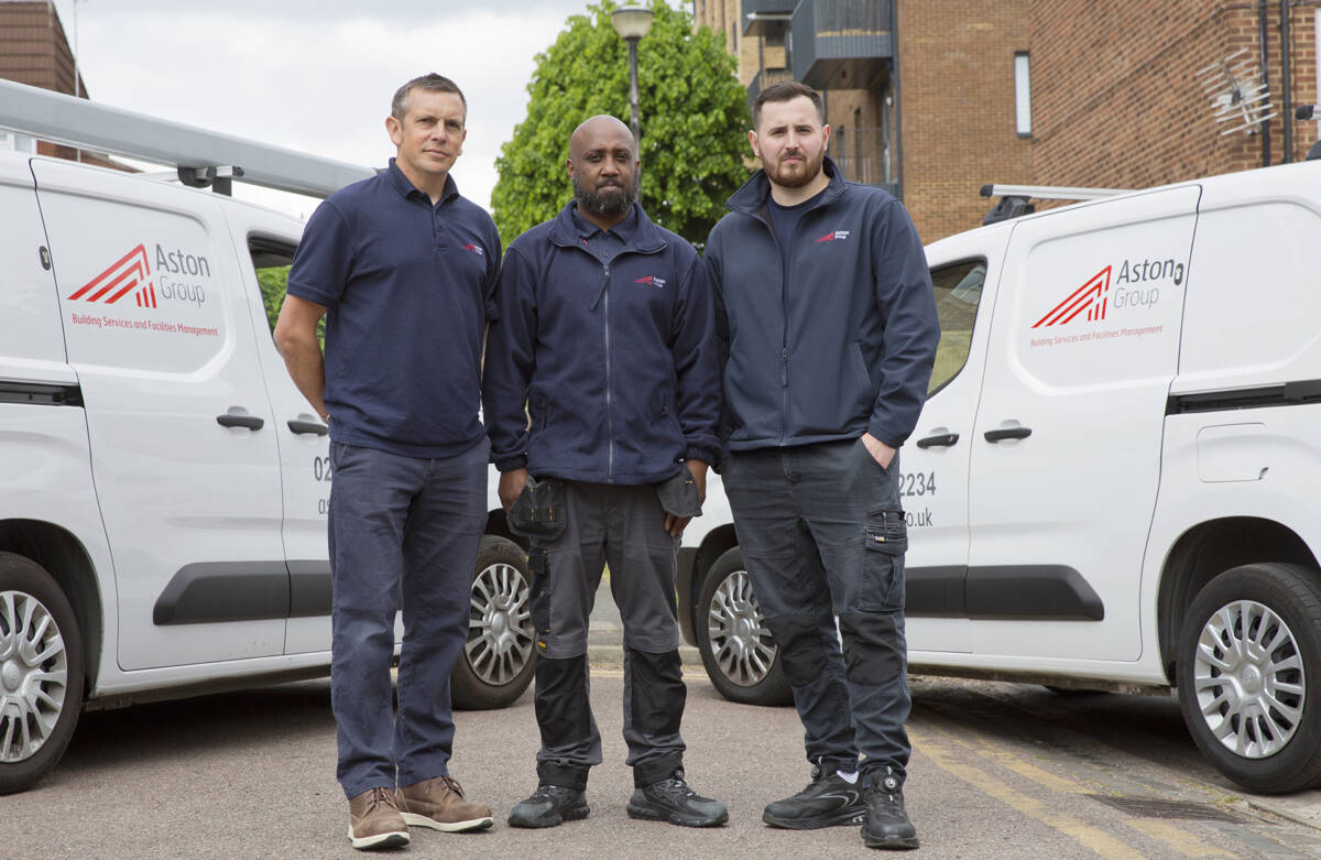 A photo of three workers standing in front of two vans