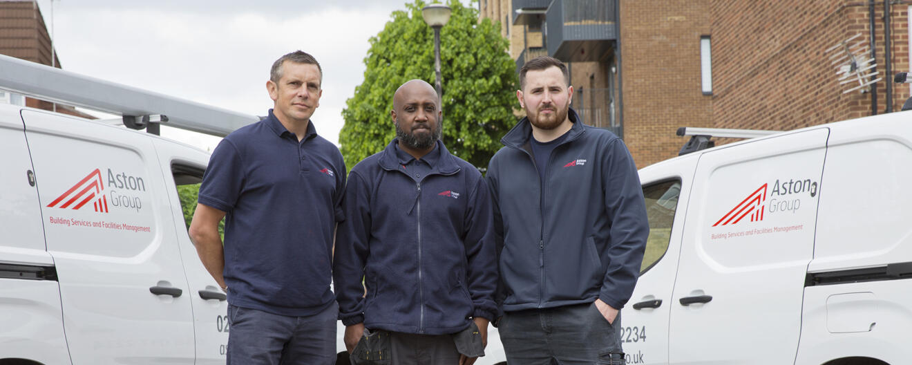 A photo of three workers standing in front of two vans